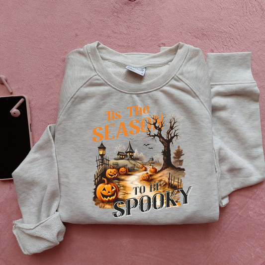 Bluza de Halloween cu textul 'Tis the Season to be Spooky', ilustrație cu dovleci luminoși și un drum care conduce către silueta unui castel bântuit